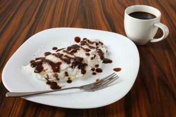 Coconut tapioca with condensed milk, coffee cup in the background. Brazilian dessert.