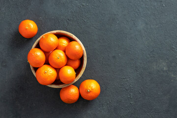 Wooden bowl of tangerine on a dark background top view with copy space