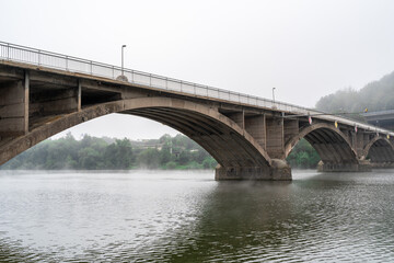 Fototapeta na wymiar Old bridge for traffic on a river with fog and cloudy sky 