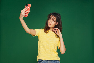 Modern young girl beauty blogger make selfie on phone, shoot photo for social network content posing on green background