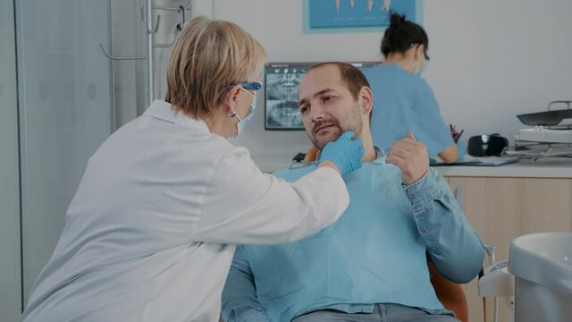 Medic consulting patient with denture problems and toothache sitting on dental chair. Stomatologist doing examination to treat man with caries, talking about surgical procedure.