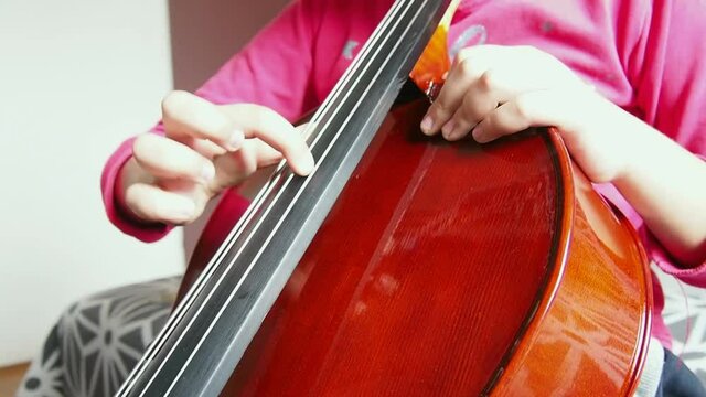 Picicato on the cello. A child girl in a pink jacket plays pizzicato with her fingers the cello without a bow. An entry-level violoncello study at a music school