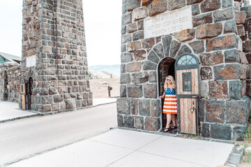 Patriotic woman wearing an American flag dress and stands in the small doorway of the Theodore Roosevelt Arch in Yellowstone National Park