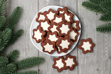 Flat lay chocolate chip cookies with white icing in the shape of stars on a gray wooden background and Christmas tree branches. Top view.