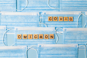 Background from blue medical masks with inscription from wooden letters OMICRON and COVID. Shot 2.