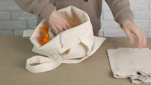 Collect cotton bags. A woman puts her cotton bags into one on the table.