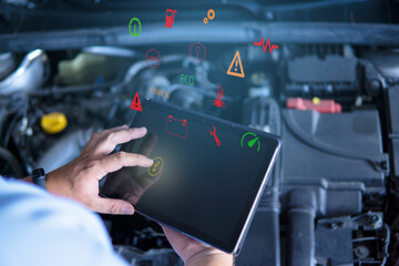 Auto mechanic with digital tablet at work making an engine repair diagnosis of a car in a mechanic garage, touching icons on virtual screen - obrazy, fototapety, plakaty