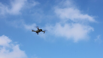 Drones fly in the air. A drone with a camera flies above the ground on a blue sky background with white clouds. selective focus