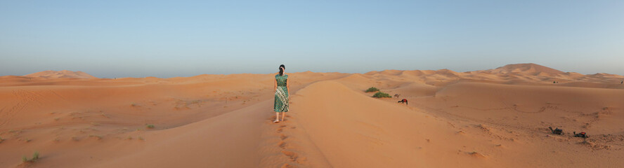 Fototapeta na wymiar Panoramic picture of Yellow, golden and arid desert view. Camel in hot Sahara. Caucasian Woman with green dress.