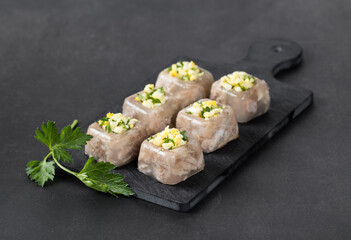 Traditional Russian festive cold appetizer. Pork jelly with pieces of meat in the form of small square portions with a filling of finely chopped egg and parsley, on a board on a dark gray background