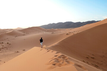 Fototapeta na wymiar Sahara desert's dunes at sundown, Man running alone in the hot dunes enjoying a great feeling of freedom