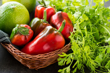 Some fresh red chili pepper and lemons in a basket with fresh coriander on a black wooden table