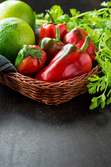 Some fresh red chili pepper and lemons in a basket with fresh coriander on a black wooden table