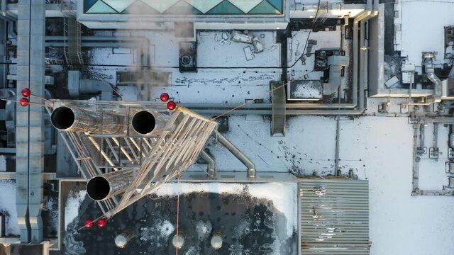 Heating, ventilation and air conditioning systems installed on a snow-covered rooftop. Smoke is coming out of the chrome-plated triple chimney. Aerial top down view