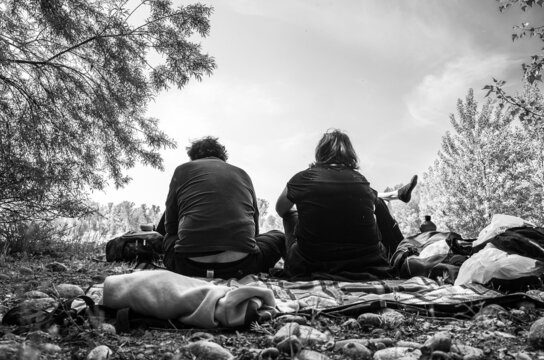 Back view of two men sitting on the ground having a picnic in nature