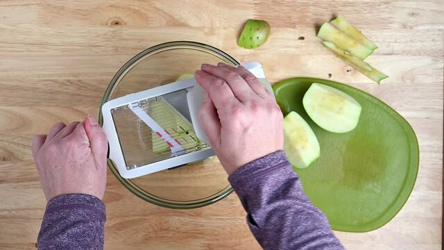 Woman&rsquo;s hands using a mandolin slicer to cut a quartered granny smith apple into slices for dehydrating
