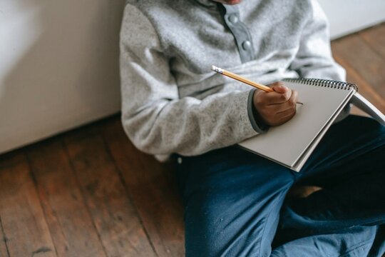 Cropped image of a boy writing on a notebook sitting on wooden floor