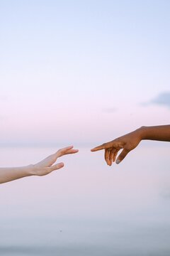 Cropped image of two hands trying to reach each other near ocean