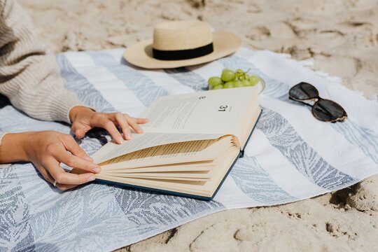 Cropped image of woman reading a book laying on textile at the beach