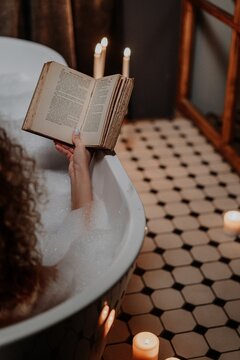 Cropped image of woman relaxing ad reading a book in the bathtub