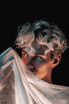 Portrait of blonde young man with textile against dark background
