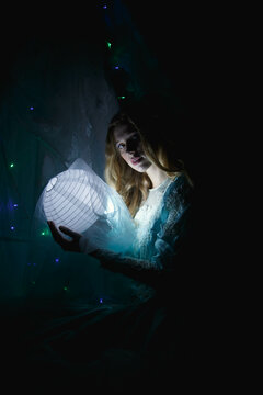 Portrait of woman in blue dress holding light paper lantern in a dark room