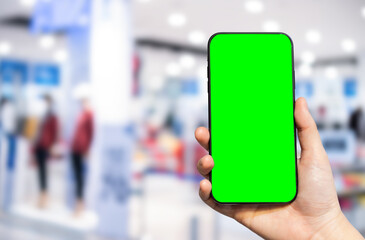 Close-up of female use Hand holding smartphone with empty blank green screen blurred images touch of Abstract blur of inside shopping complex background,shopping online concept.