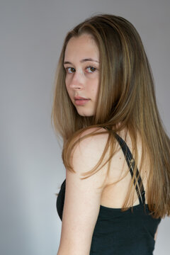 Side view of blonde teenage girl in dark strap top against light background