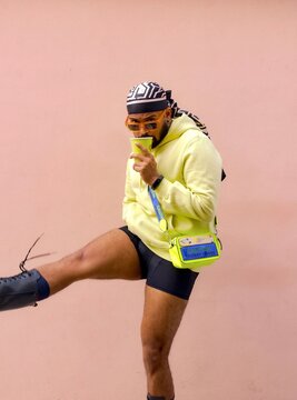 South Asian wearing bandana and eyeglasses holding a plastic cup and kicking one leg