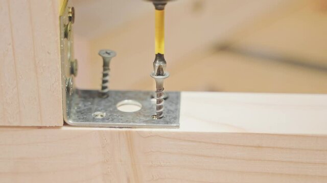 Close-up of a cross-head on a screwdriver twists screws into a wooden bar to secure a metal corner