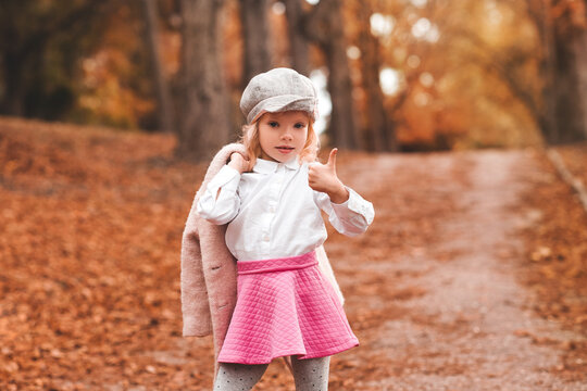 Young girl posing in pink skit and gray hat holding a jacket