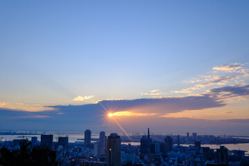 都市の夜明け。日の出の時間が過ぎるが、太陽は厚い雲に隠れていたが、ようやく雲の切れ目から顔を出す。神戸の山手ヴィーナスブリッジから撮影