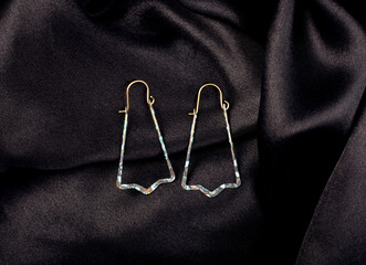 A metal earrings on black silk background.