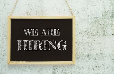 We are Hiring typography text on wooden blackboard hanging on concrete background