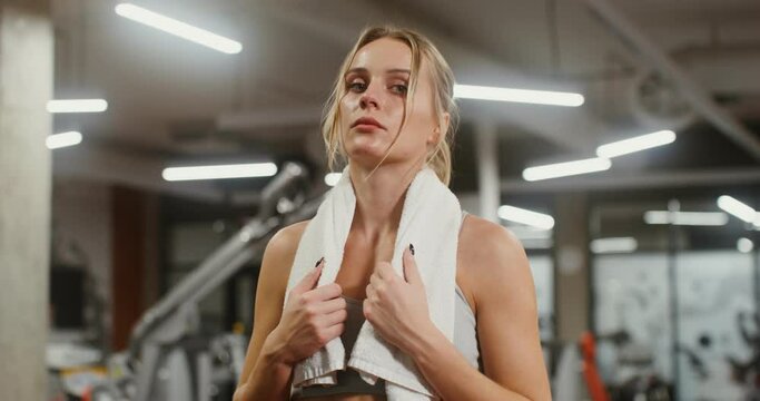 Young woman tired after training, looking at the camera while standing in gym