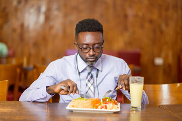 selective focus of african man, holding cutlery, food and juice in front of him on table- food...