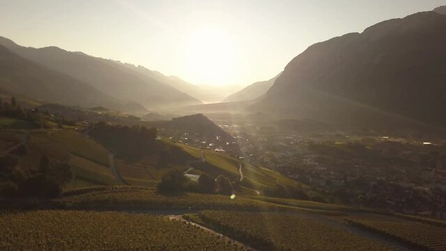 Drone shot in the early morning with the sun rising in the distance over a beautiful mountain valley in Lavaux Oron, Switzerland in 4k.
