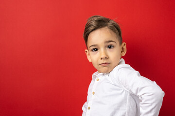 One boy male child five years old in front of red background wall wearing white shirt looking to the camera confident copy space waist up
