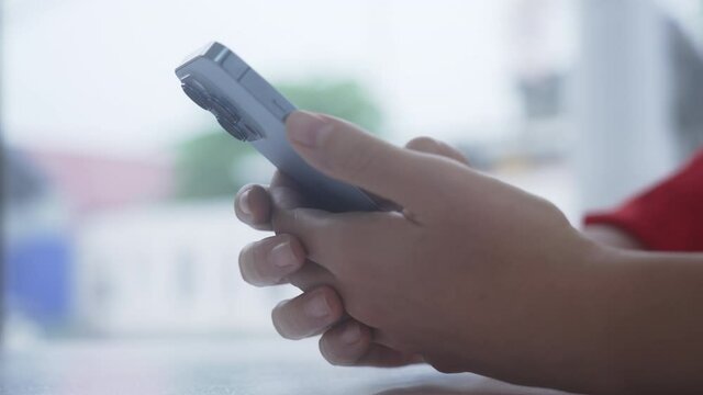Close-up of person's hands typing on text on new iphone 13 pro phone, against background of bright street with passing cars. Blogger is sitting in cafe and watching feed of social networks Slow motion