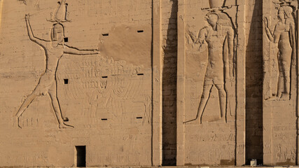 A fragment of the wall of the ancient Egyptian temple of Horus in Edfu. Figures of gods and hieroglyphs are carved on the stones. Close-up - obrazy, fototapety, plakaty