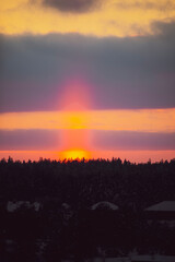 Bright orange sunset pillar in the sky. Rare optical phenomenon in winter, illuminated ice crystals in the air. Selective focus on the details, blurred background.