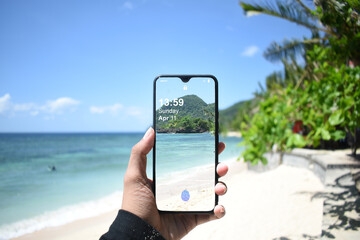 Cellphone on hand. Taking picture on the beach and white sand. 