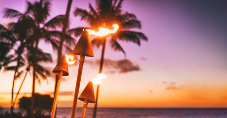 Hawaii luau beach party at sunset. Hawaiian tiki torches lighted up with fire at luxury resort hotel restaurant. Panoramic banner of hawaiian aloha spirit. - obrazy, fototapety, plakaty