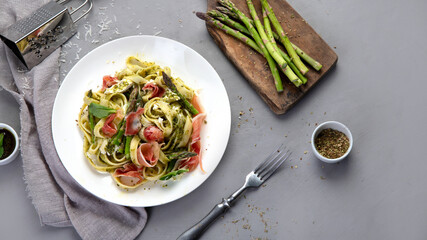 Pasta with asparagus and prosciutto on gray background.
