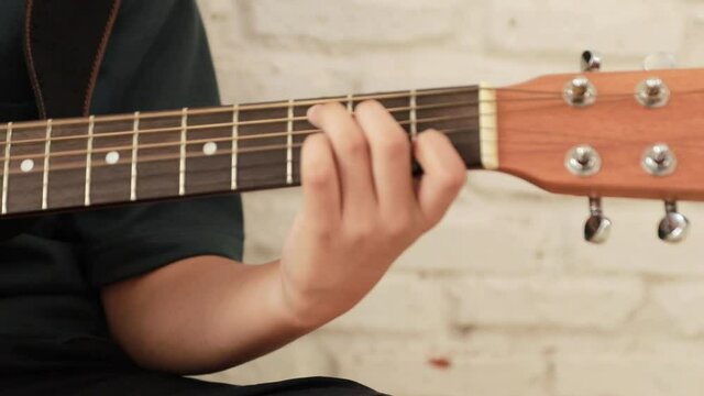 Close-up of young man's hands practicing acoustic guitar at home.