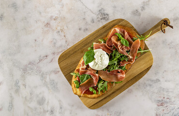 Pinsa Romana or homemade pizza with Italian meat, burrata cheese, tomatoes, and arugula. Made from wheat flour, rice flour, and soy flour. Top view, copy space for the recipe.