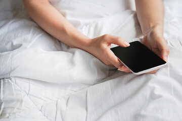 Woman's hand holding phone with black blank screen on bed. Clipping path.