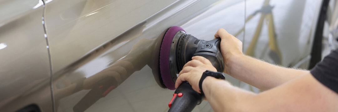 Master repairman polishing car door using special machine in workshop closeup
