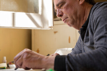 Fototapeta premium Concentrated Senior man drawing a pastel sketch at home studio while daylight gets into a window