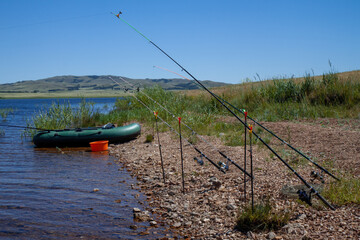 Several fishing rods and rubber boat on the shore of the lake.